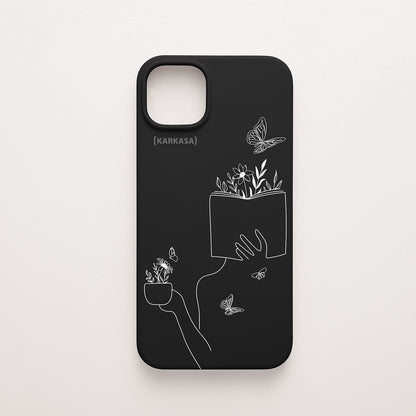 Funda de móvil KARKASA con ilustración lineal blanca de una figura leyendo con flores y mariposas, en silicona mate Silk Touch negra.