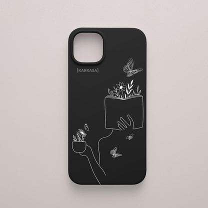 Funda de móvil KARKASA con ilustración lineal blanca de una figura leyendo con flores y mariposas, en silicona mate Silk Touch negra.